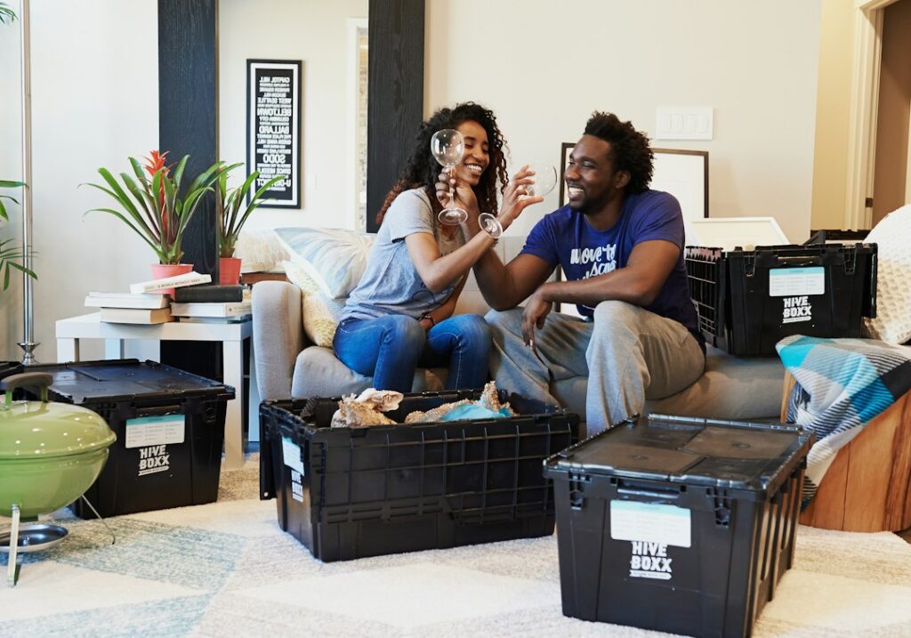 A couple celebrating on a sofa surrounded by moving boxes in their new home